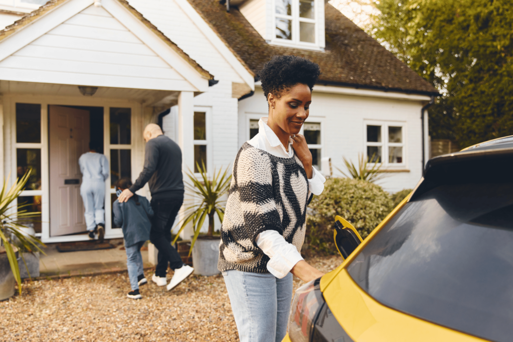 A woman in front of a home, plugging in an electric vehicle to charge.